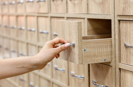 A person is reaching into a wooden drawer. The drawer is part of a large wooden cabinet. The cabinet is full of drawers and has a rustic, old-fashioned lookの写真素材