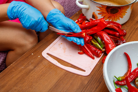 A woman is cutting red peppers on a cutting board. There are two bowls of peppers on the tableの写真素材