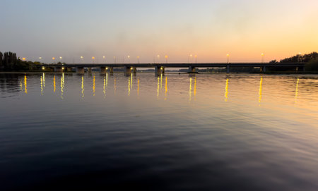 A bridge spans a river at sunset. The water is calm and the sky is a beautiful mix of orange and pink huesの写真素材