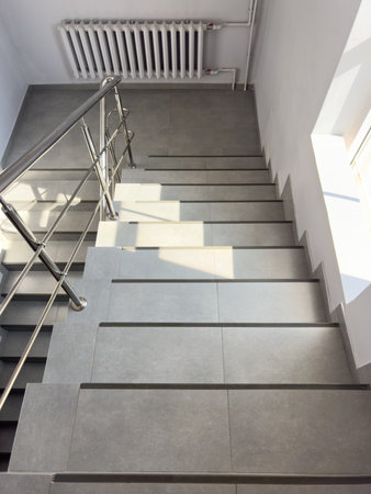 A staircase with a metal railing and a radiator above it. The stairs are gray and the railing is...