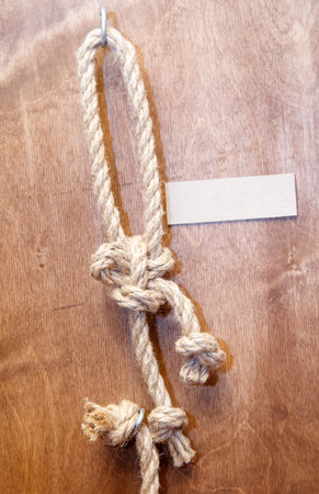 A rope is tied to a hook on a wooden surface. The rope is made of a material that is strong and...