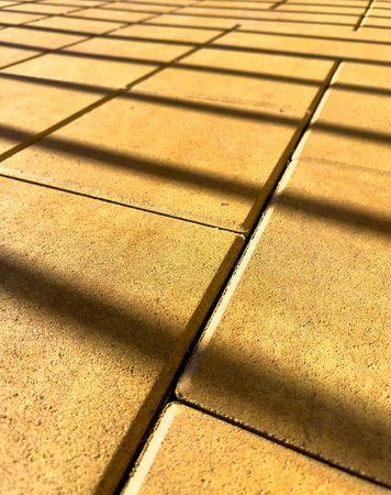 A close up of a tan brick floor with a shadow cast on it. The shadow is dark and elongated, creating a sense of depth and dimensionの写真素材
