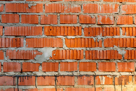 A brick wall with a few holes and some paint on it. The wall is red and has a rough textureの写真素材
