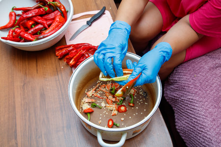 A woman is cutting red peppers on a cutting board. There are two bowls of peppers on the tableの写真素材