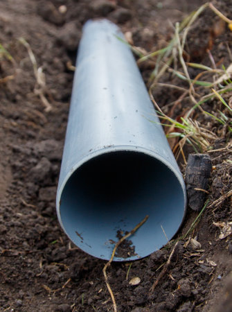 A gray pipe is laying in the dirt. The pipe is long and narrow. The dirt is brown and the grass is...