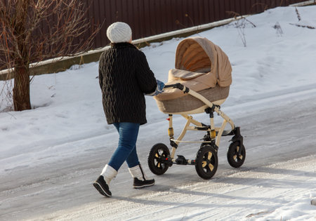 A woman is pushing a stroller on a snowy road. The scene is quiet and peaceful, with the woman and...