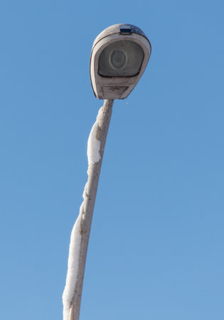 A street light is covered in snow and is lit up. The light is on a pole and is lit up in the blue skyの写真素材