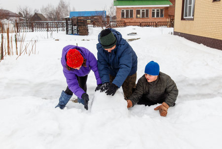 A man and two children are playing in the snow. The man is helping the children build a snowmanの写真素材