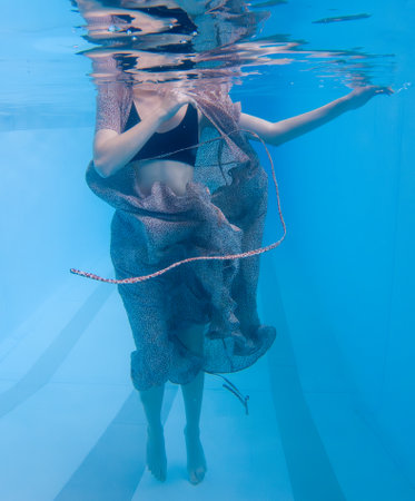 A woman is in a pool wearing a dress and holding a rope. The image has a mood of elegance and sophisticationの写真素材