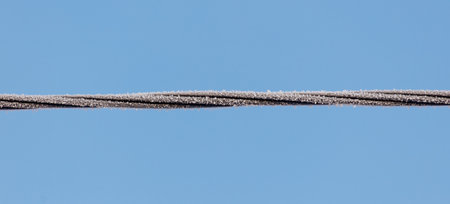A wire is shown in the sky with a blue background. The wire is covered in ice and snow