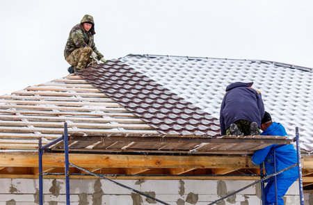 A man is working on a roof with two other men. The roof is covered in snow and the men are trying to clear itの写真素材
