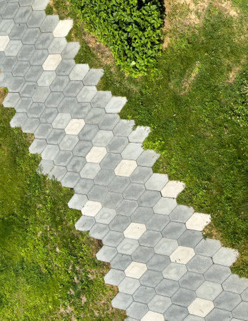 A gray and white path with a green grassy area in the background. The path is made of small tiles...
