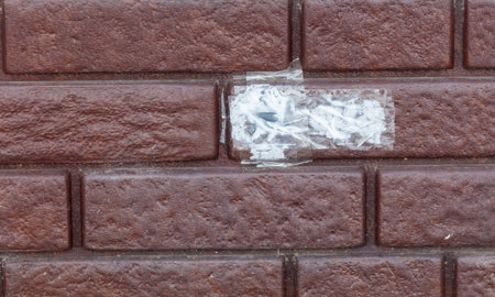 A brick wall with a white sticker on it that is shaped like a brick. The sticker is placed in the middle of the wall. The wall is made of red bricksの写真素材