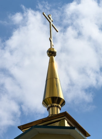 A gold cross is on top of a building. The sky is blue and there are clouds in the backgroundの写真素材