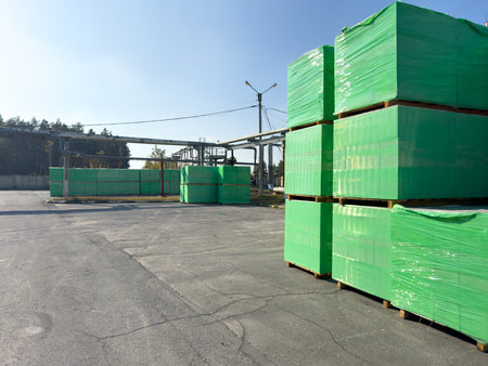 A pile of green plywood is stacked in a lot. The plywood is wrapped in plastic and is ready to be usedの写真素材