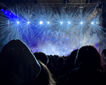 A crowd of people are watching a concert with lights shining on them. Scene is energetic and excitingの写真素材
