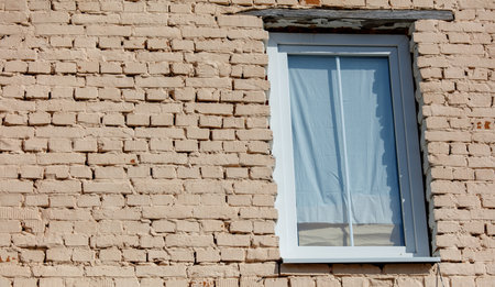A small window with a white curtain is framed by a brick wall. The curtain is drawn, and the window...
