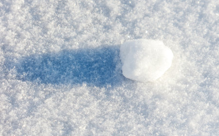 A snowflake is sitting on top of a snow covered ground. The snowflake is small and white