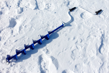 A blue ice auger is sitting in the snow, with the snow being white and the ice auger being blueの写真素材