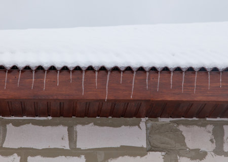 A roof covered in snow and icicles. The roof is wooden and the snow is piled up on it