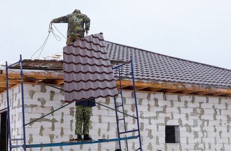 A man in camouflage is on a ladder, fixing a roof. Concept of hard work and dedication to completing a taskの写真素材