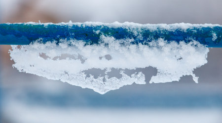 A blue metal pole covered in snow. The snow is piled up on the pole and it looks like it's about to...