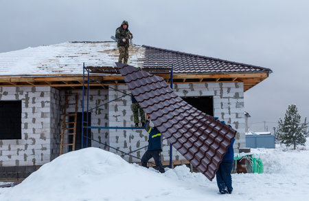 A man is holding a piece of roofing material while two other men are working on a houseの写真素材