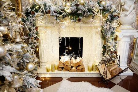 A fireplace with a white mantle and a Christmas tree in the background. The mantle is decorated with white and gold ornamentsの写真素材
