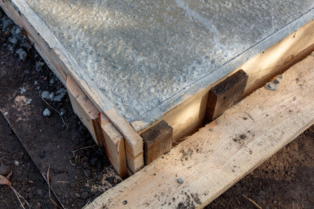 A wooden plank is being used to hold a concrete slab in place. The slab is being poured into a hole in the groundの写真素材