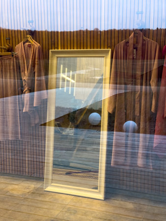 A mirror is on the wall in front of a store window. The mirror is reflecting the store window and the clothes hanging on the clotheslineの写真素材