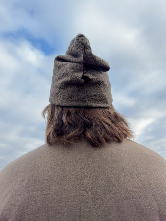 A man wearing a hat with a brown color. The hat is on his head and it is a cloudy day