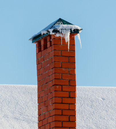 A brick chimney with icicles on top. The chimney is tall and the icicles are hanging from the top. The image has a cold and wintry moodの写真素材