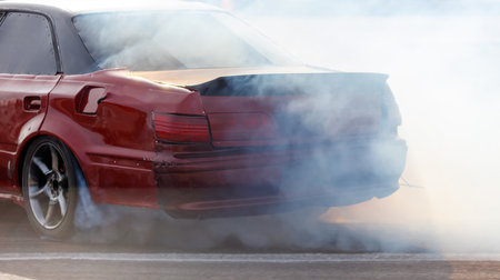 A red car is driving with smoke coming out of the back. The car is making a lot of noise and is leaving a trail of smoke behind itの写真素材