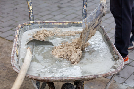 A person is shoveling sand into a wheelbarrow. The wheelbarrow is full of sand and the person is using a shovel to fill itの写真素材