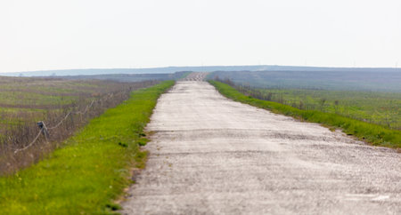 A long, empty road with a fence on the side. The road is mostly empty, with only a few cars visible...