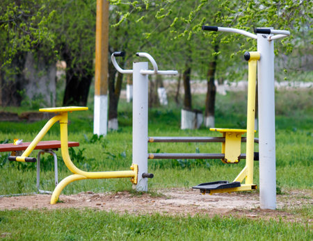 A park with a yellow and white exercise machine. The machine is surrounded by a bench and a fenceの写真素材
