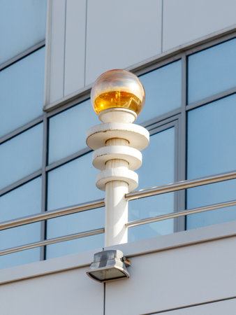 A tall white pole with a yellow ball on top. The pole is on a balcony and the ball is lit upの写真素材