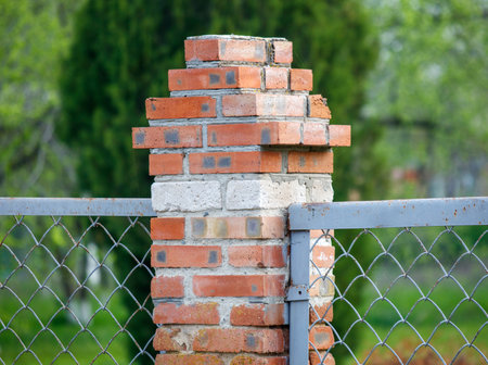 A brick wall with a broken brick and a chain link fence. The fence is rusted and the brick wall is in a state of disrepairの写真素材