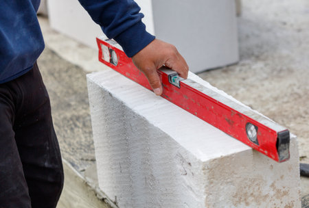 A man is holding a red level in his hand. He is standing in front of a white blockの写真素材