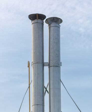 Two tall metal pipes with a yellow pipe attached to them. The pipes are connected to a chimneyの写真素材