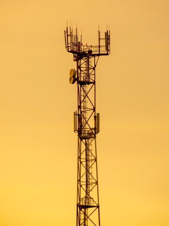 A tall tower with a lot of antennas on it. The tower is yellow and the sky is orangeの写真素材