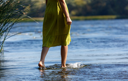 A woman is walking in the water wearing a green dress. The water is calm and clear, and the woman's...