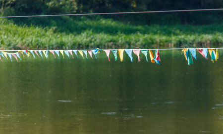 A row of colorful flags hanging over a body of water. The flags are of different colors and sizes, and they are tied to a wire. The scene has a peaceful and serene moodの写真素材