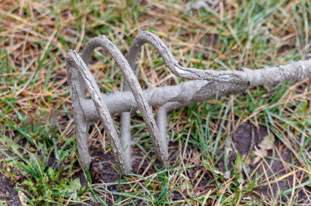 A rusty, old metal object is laying on the ground. It is a tool or a piece of equipment. The object is surrounded by grass and dirt, giving it a somewhat abandoned and neglected appearanceの写真素材