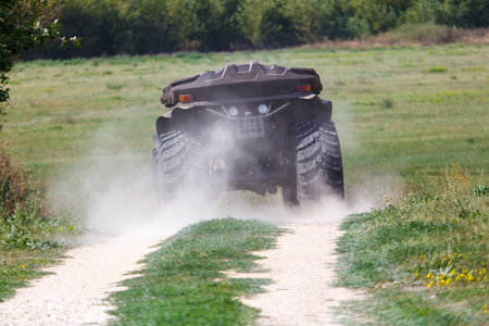 A large, dirty, muddy, and dusty monster truck is driving down a dirt road. The truck is covered in...