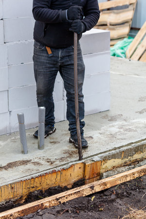 A man is standing in front of a pile of bricks, holding a metal rod. The scene is somewhat chaotic, with the man's focus on the task at hand. Scene is determined and focusedの写真素材