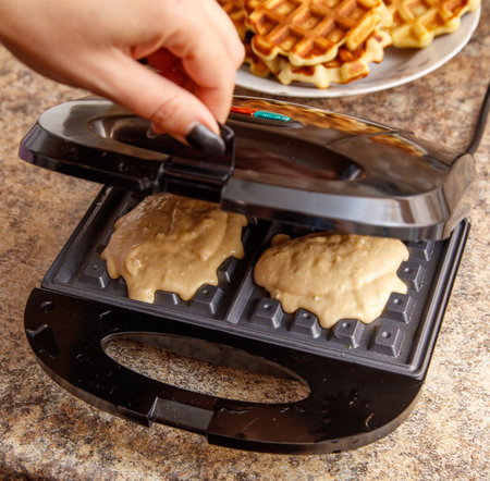 A person is making waffles in a waffle maker. The waffles are in the process of being cooked