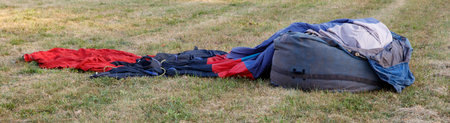 A pile of clothes and a bag are on the grass. The clothes are red, blue, and blackの写真素材