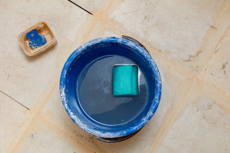 A blue bucket filled with water and a green sponge. The bucket is on a tile floorの写真素材