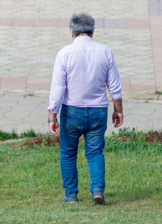 A man in a purple shirt and blue jeans walks across a grassy field. The man is alone and is looking ahead. The scene is peaceful and calmの写真素材